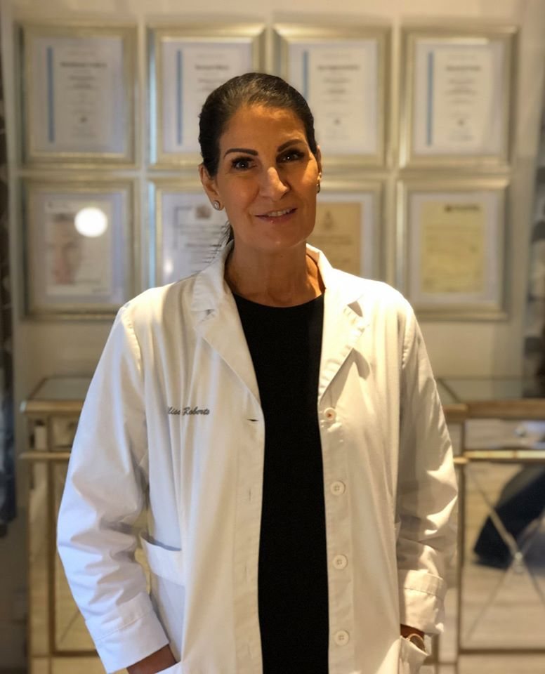 Allison McCarron in her white clinic coat in front of her framed qualifications
